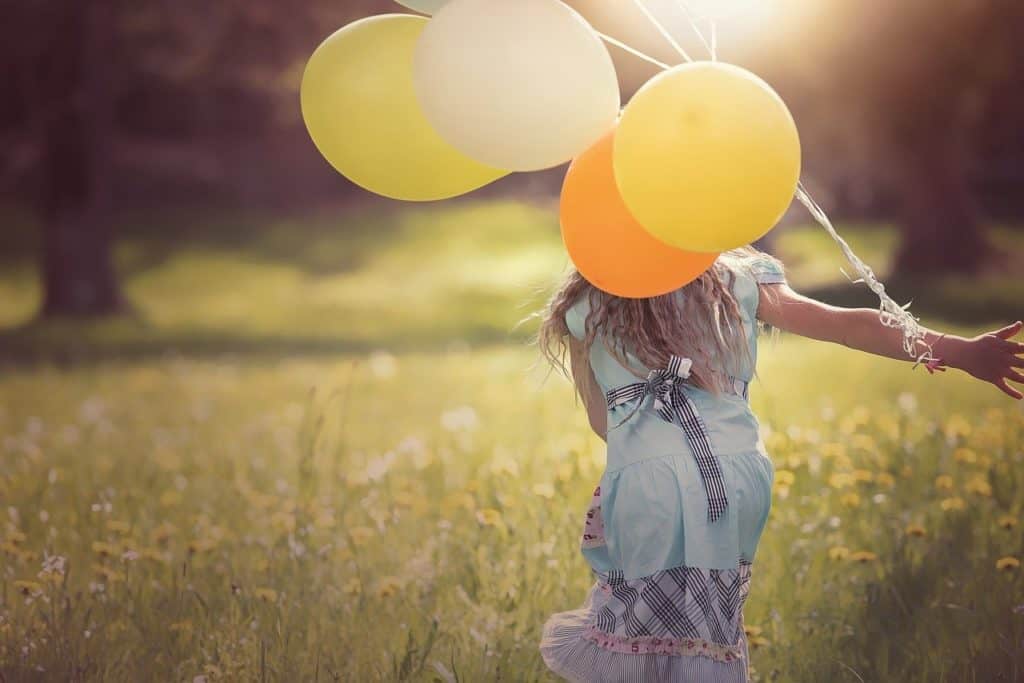 Girl running with balloons in a field.