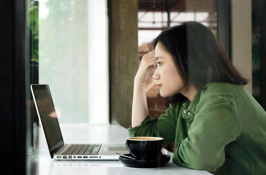 Woman looking pensively at open laptop. From the article "Staying productive as a writer" available on Dreamers Creative Writing.