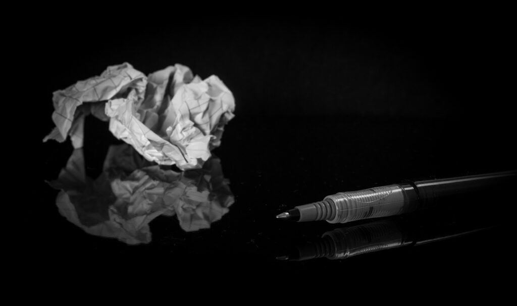 Crumpled paper in a ball beside a pen representing writer’s block.